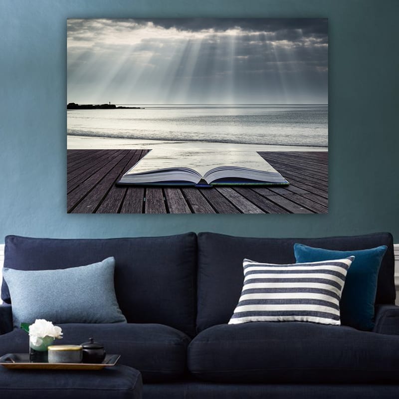 Lerretsbilde 70x100 cm - Åpen bok liggende på en trebrygge ved sjøen, omgitt av myke lysstråler fra en overskyet himmel - Grå / Blå / Hvit - Innredning - Bilder & kunst - Lerretsbilder