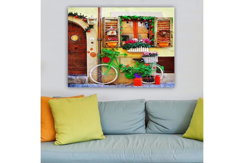 Lerretsbilde 70x100 cm - Fargerik sykkel pyntet med blomster og potter foran en sjarmerende vegg med vinduer og dekorasjoner - Grønn / Rosa / Oransje - Innredning - Bilder & kunst - Lerretsbilder