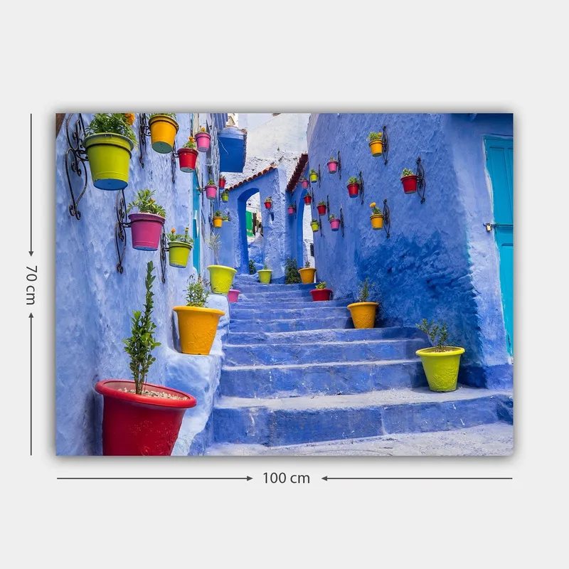 Lerretsbilde 70x100 cm - Fargerik trapp omgitt av blomsterpotter i et pittoresk, blått bymiljø - Blå / Gul / Rød - Innredning - Bilder & kunst - Lerretsbilder