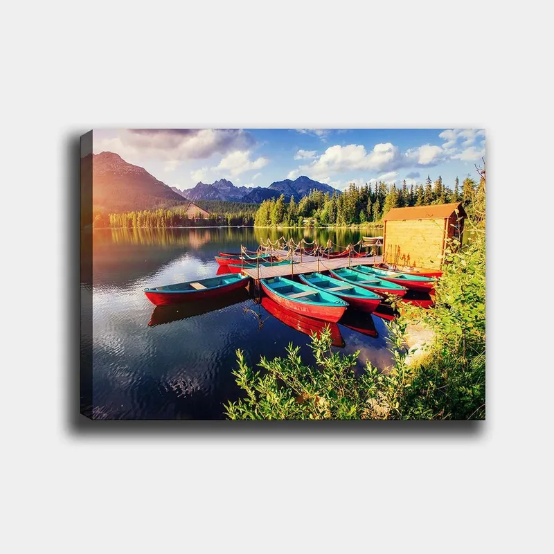 Lerretsbilde 70x100 cm - Flere fargerike båter ligger på en speilblank innsjø omgitt av frodige trær og fjell, Rød / Turkis / Grønn