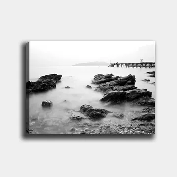 Lerretsbilde 70x100 cm - Fredelig kystlandskap med klipper og en brygge i det fjerne - Svart / Hvit / Grå - Innredning - Bilder & kunst - Lerretsbilder