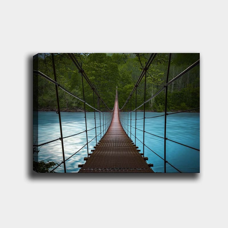 Lerretsbilde 70x100 cm - Hengebro som går over en rolig, blå elv omgitt av frodige trær, Mørk brun / Turkis / Grønn