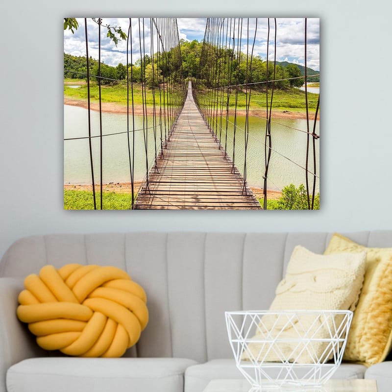 Lerretsbilde 70x100 cm - Hengebro som går over en rolig innsjø, omgitt av frodig grøntområde - Grønn / Brun / Blå - Innredning - Bilder & kunst - Lerretsbilder