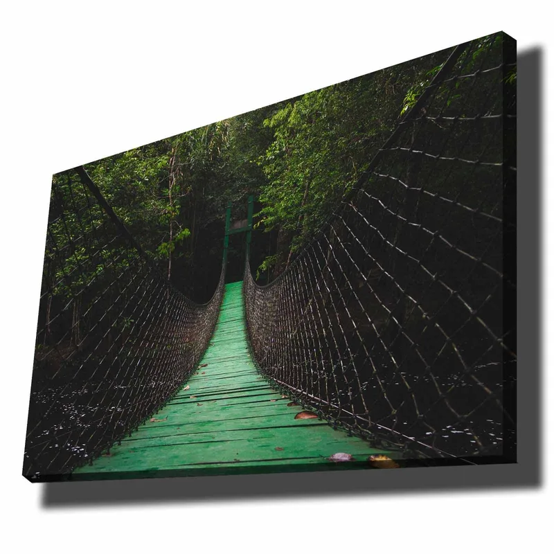 Lerretsbilde 70x100 cm - Hengebro som strekker seg gjennom en frodig skog, Grønn / Svart