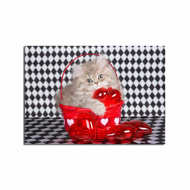 Lerretsbilde 70x100 cm - Kattunge sitter i en rød kurv fylt med hjerteformede dekorasjoner, Rød / Grå