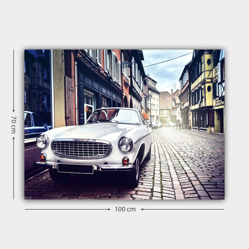 Lerretsbilde 70x100 cm - Klassisk hvit bil parkert i en sjarmerende, gammeldags gate med historiske bygninger - Hvit / Svart / Grå - Innredning - Bilder & kunst - Lerretsbilder