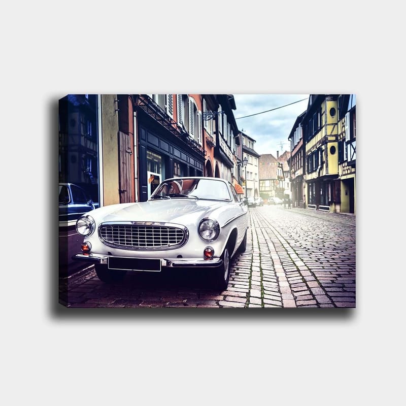 Lerretsbilde 70x100 cm - Klassisk hvit bil parkert i en sjarmerende, gammeldags gate med historiske bygninger, Hvit / Svart / Grå