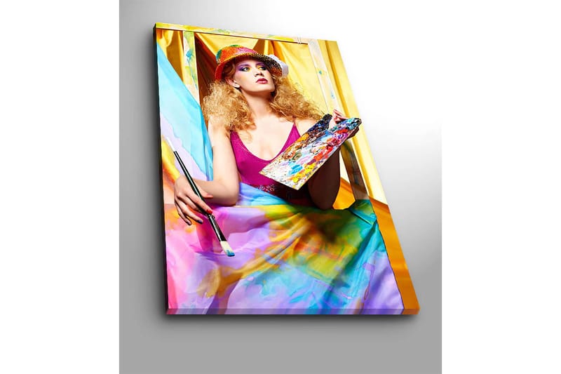Lerretsbilde 70x100 cm - Kreativ kvinne som maler med en palett i hånden, omgitt av fargerike stoffer - Rosa / Blå / Gul - Innredning - Bilder & kunst - Lerretsbilder
