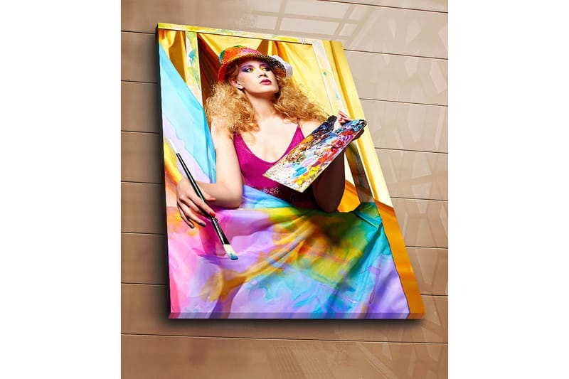 Lerretsbilde 70x100 cm - Kreativ kvinne som maler med en palett i hånden, omgitt av fargerike stoffer - Rosa / Blå / Gul - Innredning - Bilder & kunst - Lerretsbilder
