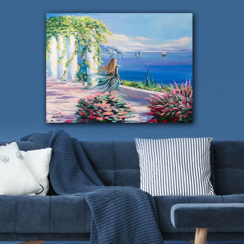 Lerretsbilde 70x100 cm - Kvinne i blå kjole som står ved et utsiktspunkt med havet og seilbåter i bakgrunnen - Blå / Grønn / Rosa - Innredning - Bilder & kunst - Lerretsbilder