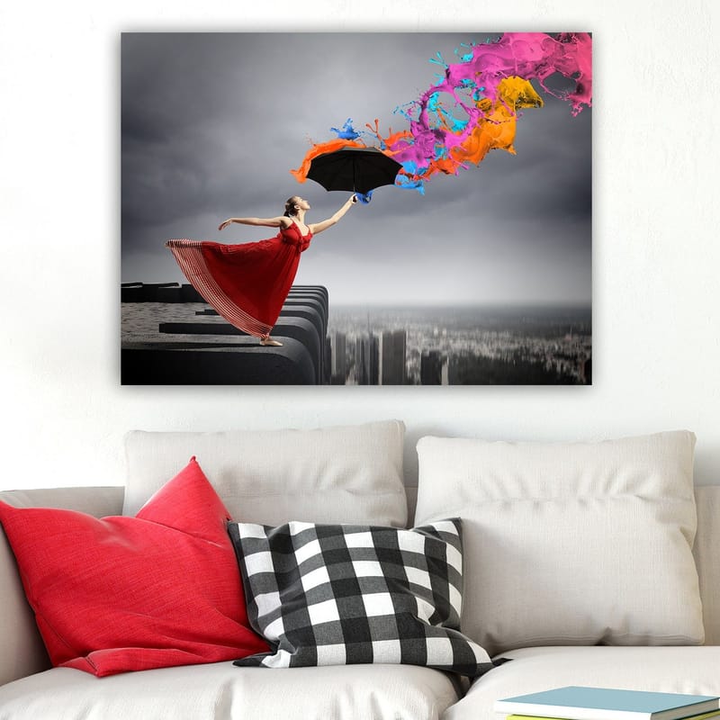 Lerretsbilde 70x100 cm - Kvinne i rød kjole står på en kant og holder en paraply, mens fargerike malingsstråler spruter ut fra den - Rød / Svart / Oransje - Innredning - Bilder & kunst - Lerretsbilder