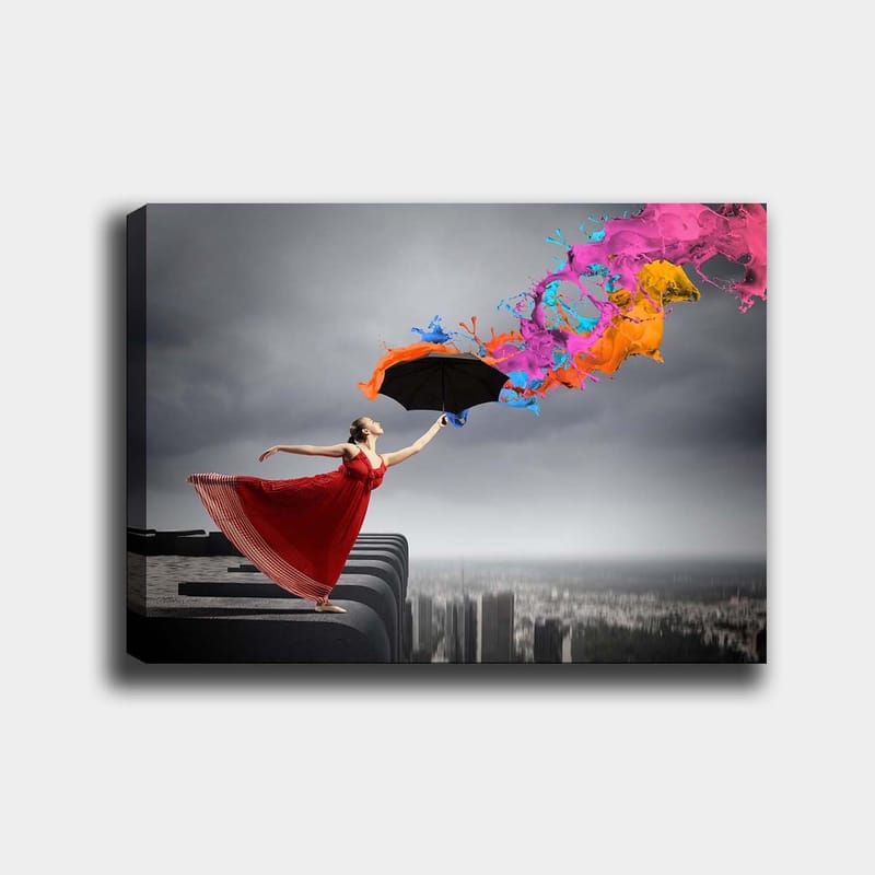 Lerretsbilde 70x100 cm - Kvinne i rød kjole står på en kant og holder en paraply, mens fargerike malingsstråler spruter ut fra den, Rød / Svart / Oransje