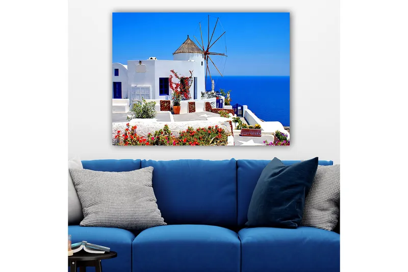 Lerretsbilde 70x100 cm - Malerisk utsikt over en hvitkalket bygning med en tradisjonell vindmølle og fargerike blomster på Santorini - Hvit / Blå / Rød - Innredning - Bilder & kunst - Lerretsbilder