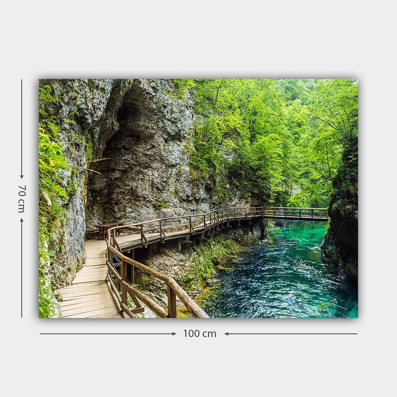 Lerretsbilde 70x100 cm - Naturskjønn utsikt over en trebro som slynger seg gjennom en frodig kløft ved en klar, turkis elv - Grønn / Turkis / Grå - Innredning - Bilder & kunst - Lerretsbilder