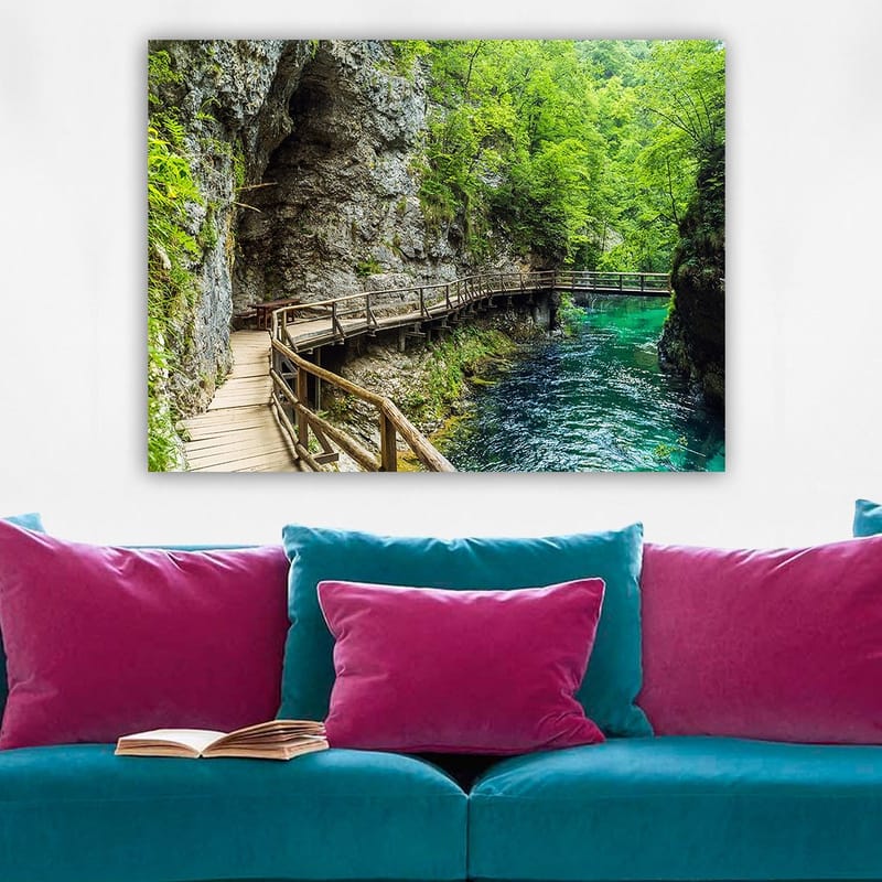 Lerretsbilde 70x100 cm - Naturskjønn utsikt over en trebro som slynger seg gjennom en frodig kløft ved en klar, turkis elv - Grønn / Turkis / Grå - Innredning - Bilder & kunst - Lerretsbilder