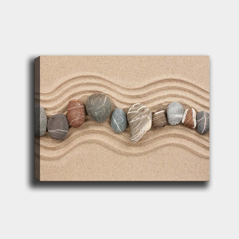 Lerretsbilde 70x100 cm - Rad med glatte steiner plassert på en sandoverflate med bølgete mønstre, Sandbeige / Grå / Rødbrun