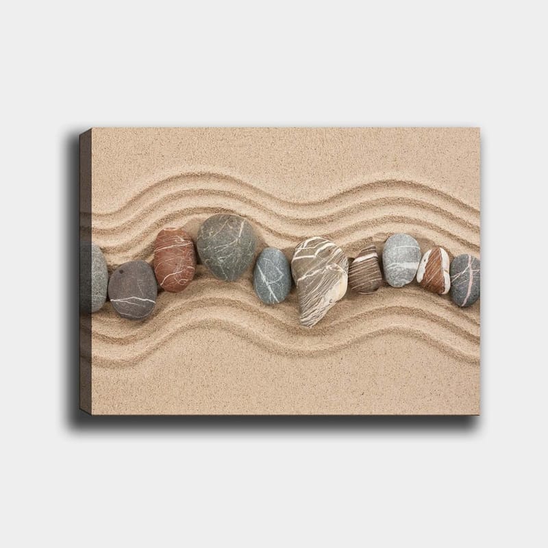 Lerretsbilde 70x100 cm - Rad med glatte steiner plassert på en sandoverflate med bølgete mønstre, Sandbeige / Grå / Rødbrun