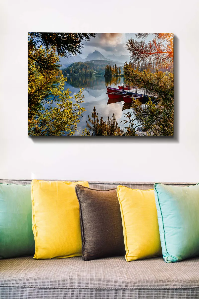 Lerretsbilde 70x100 cm - Rolig innsjø med en rød båt ved en trebrygge, omgitt av frodige trær og fjerne fjell - Grønn / Rød / Blå - Innredning - Bilder & kunst - Lerretsbilder