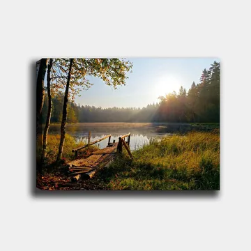 Lerretsbilde 70x100 cm - Rolig innsjø med en trebro omgitt av frodige trær og morgensolens stråler - Grønn / Brun / Gul - Innredning - Bilder & kunst - Lerretsbilder