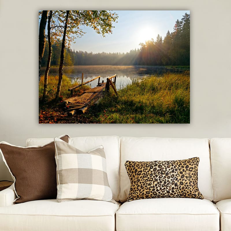 Lerretsbilde 70x100 cm - Rolig innsjø med en trebro omgitt av frodige trær og morgensolens stråler - Grønn / Brun / Gul - Innredning - Bilder & kunst - Lerretsbilder