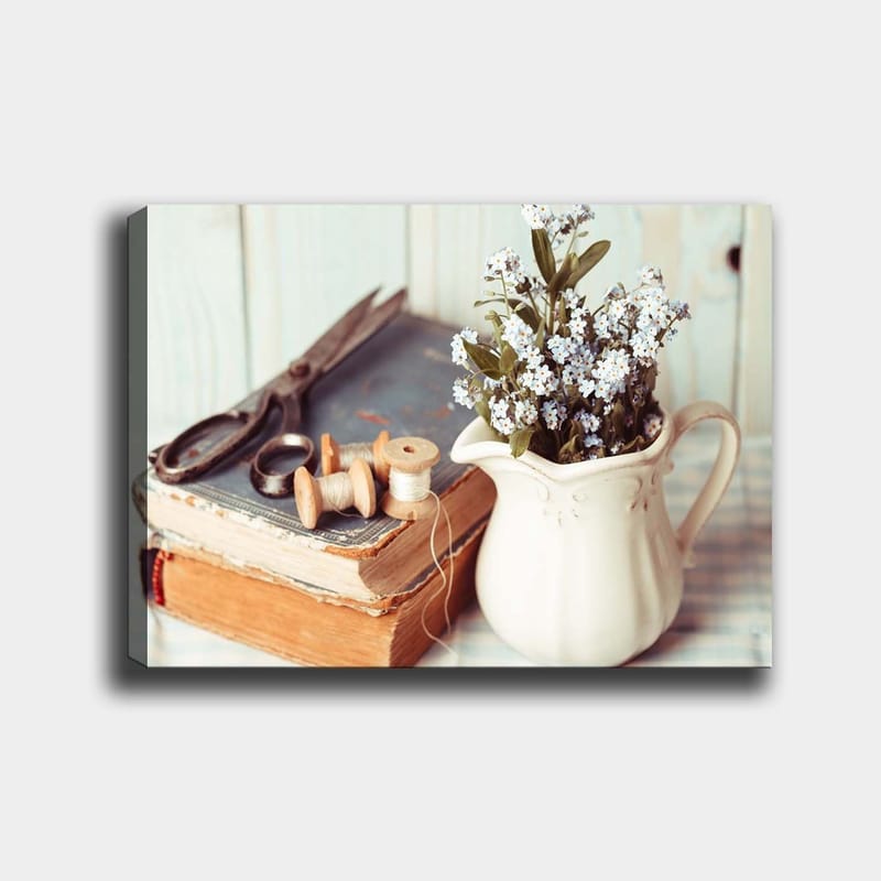 Lerretsbilde 70x100 cm - Rolig komposisjon av en mugge med blomster, en bok og syverktøy, Lys blå / Beige / Grønn