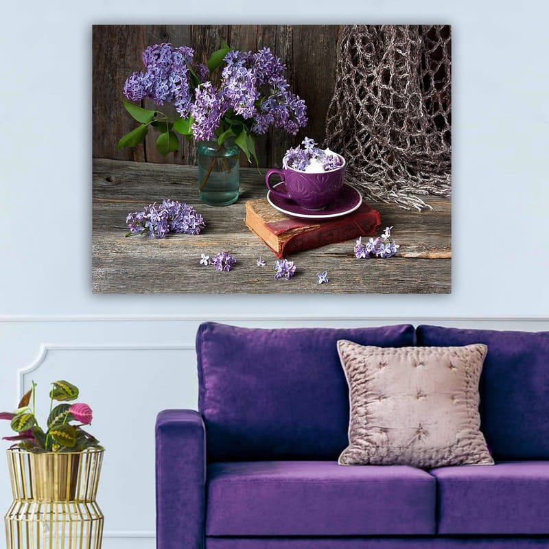 Lerretsbilde 70x100 cm - Rolig naturmaleri med lilla syriner i en glassvase og en lilla kopp på en gammel bok, Lilla / Grønn / Brun