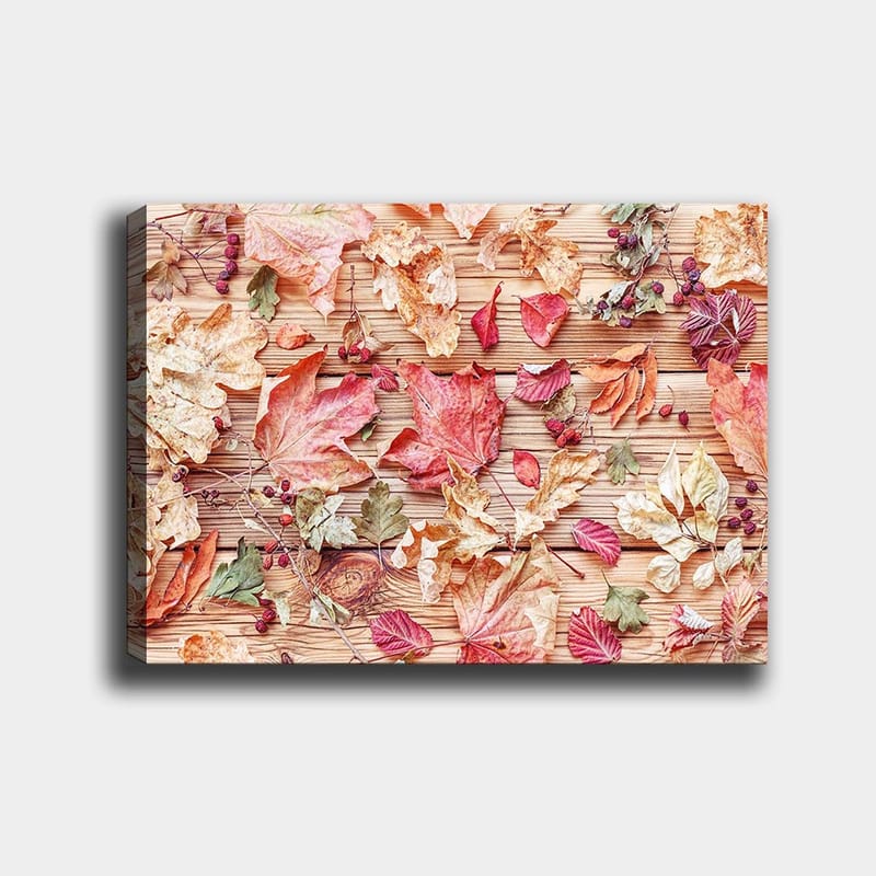 Lerretsbilde 70x100 cm - Samling av høstblader i forskjellige farger som ligger på en treflate - Rød / Gul / Grønn - Innredning - Bilder & kunst - Lerretsbilder
