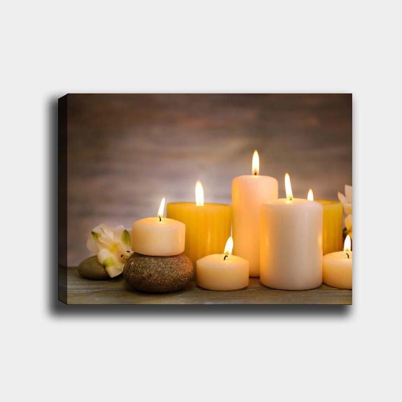 Lerretsbilde 70x100 cm - Samling av tente lys i forskjellige former og størrelser, omgitt av steiner og en blomst, Gul / Hvit / Beige