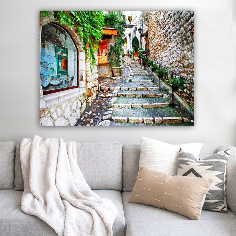 Lerretsbilde 70x100 cm - Sjarmerende smug med steiner og grøntområder som fører oppover, omgitt av historiske bygninger - Grønn / Beige / Oransje - Innredning - Bilder & kunst - Lerretsbilder