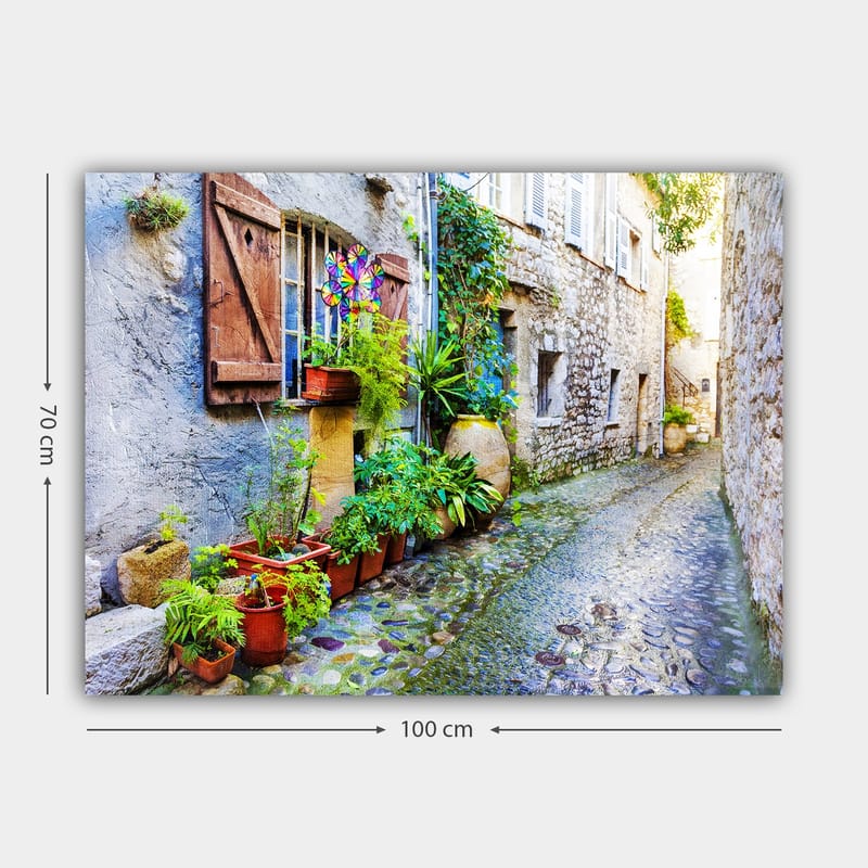 Lerretsbilde 70x100 cm - Sjarmerende smug med steinhus og blomsterpotter som skaper en livlig atmosfære - Grønn / Blå / Beige - Innredning - Bilder & kunst - Lerretsbilder