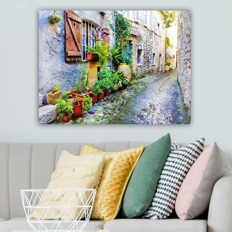 Lerretsbilde 70x100 cm - Sjarmerende smug med steinhus og blomsterpotter som skaper en livlig atmosfære - Grønn / Blå / Beige - Innredning - Bilder & kunst - Lerretsbilder