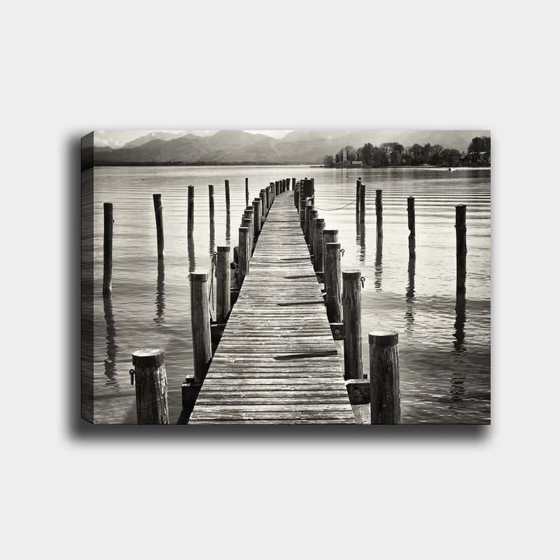 Lerretsbilde 70x100 cm - Stille brygge som strekker seg ut over vannet, omgitt av søyler som speiler seg i overflaten, Svart / Hvit / Grå