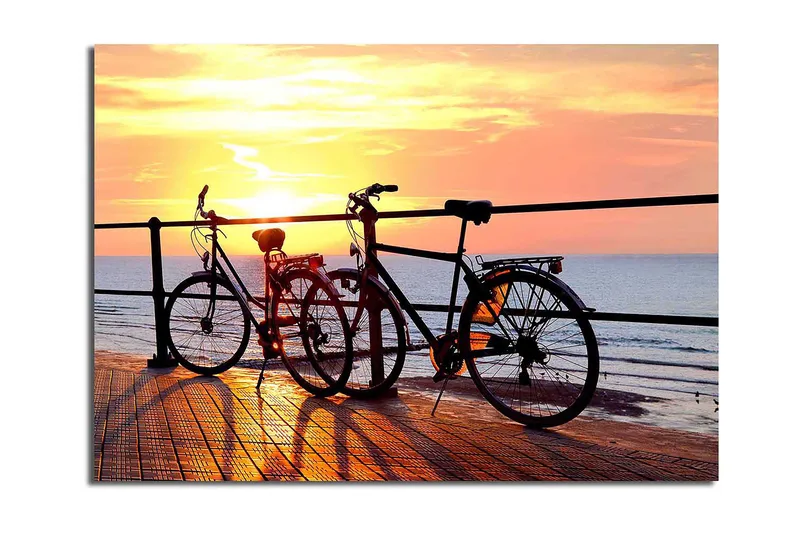 Lerretsbilde 70x100 cm - To sykler som står på en brygge ved solnedgang over havet - Oransje / Svart / Gul - Innredning - Bilder & kunst - Lerretsbilder