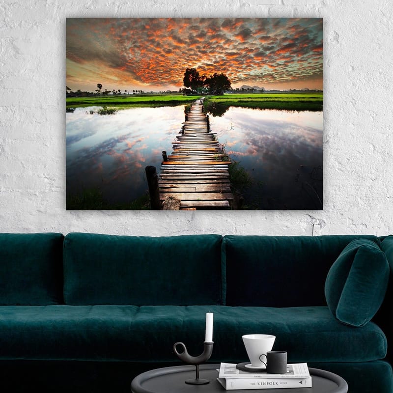 Lerretsbilde 70x100 cm - Trebro som spenner over en speilblank vannoverflate, omgitt av frodig grøntområde og en dramatisk solnedgang - Oransje / Grønn / Blå - Innredning - Bilder & kunst - Lerretsbilder