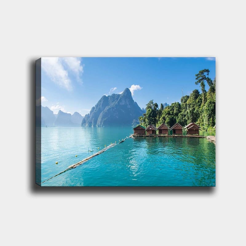 Lerretsbilde 70x100 cm - Vakker innsjø med hytter ved vannet, omgitt av majestetiske fjell og frodig skog, Turkis / Grønn / Brun