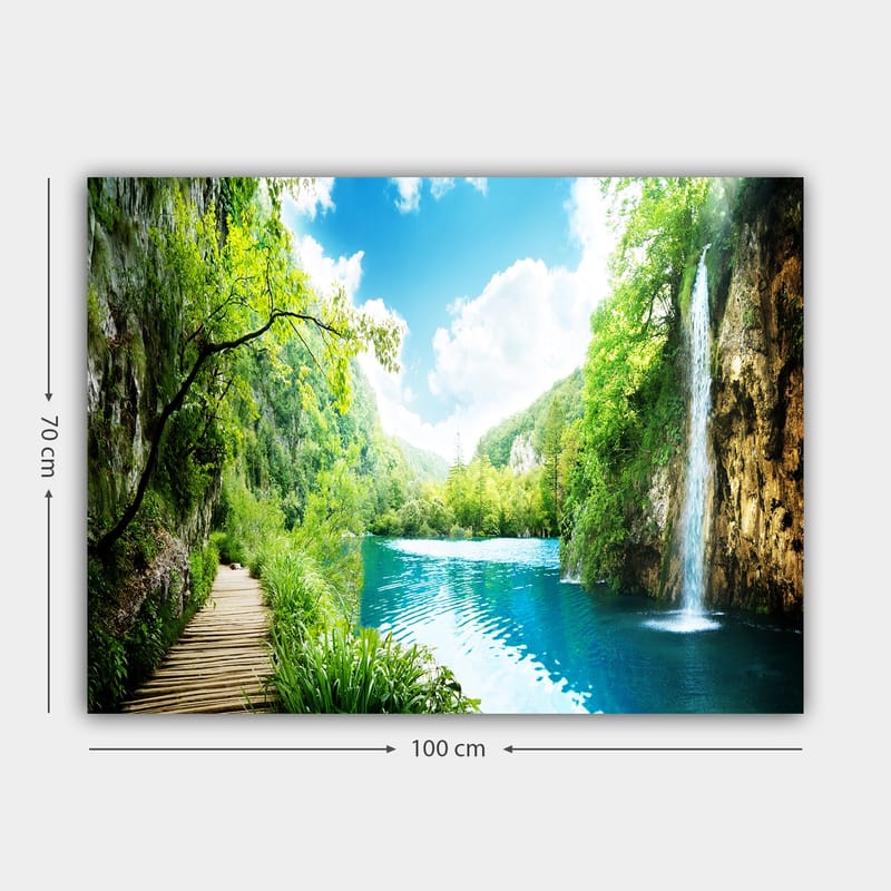 Lerretsbilde 70x100 cm - Vakker naturscene med en foss som renner ut i en klar, blå innsjø omgitt av frodig grøntområde og fjell - Grønn / Blå - Innredning - Bilder & kunst - Lerretsbilder