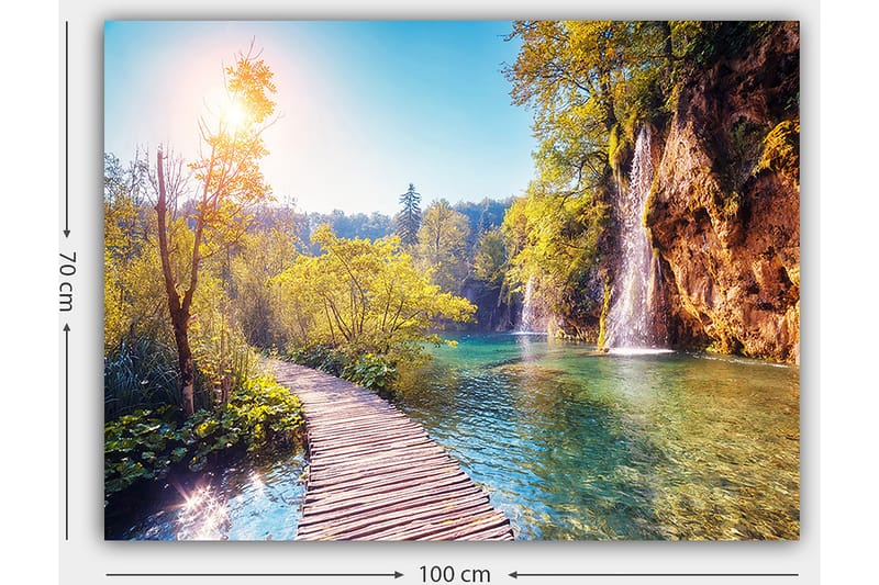 Lerretsbilde 70x100 cm - Vakker naturutsikt med en trebro som fører gjennom frodig grøntområde og en foss i bakgrunnen - Grønn / Blå / Gul - Innredning - Bilder & kunst - Lerretsbilder