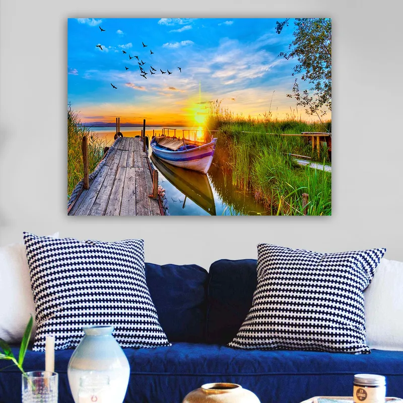 Lerretsbilde 70x100 cm - Vakker solnedgang over en rolig innsjø med en båt ved en trebrygge omgitt av grøntområder - Blå / Oransje / Grønn - Innredning - Bilder & kunst - Lerretsbilder