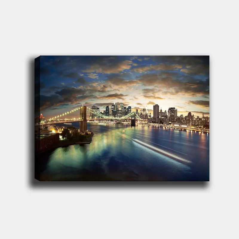 Lerretsbilde 70x100 cm - Vakker utsikt over en by med en bro som går over en glitrende elv i skumringen, Blå / Grønn / Oransje