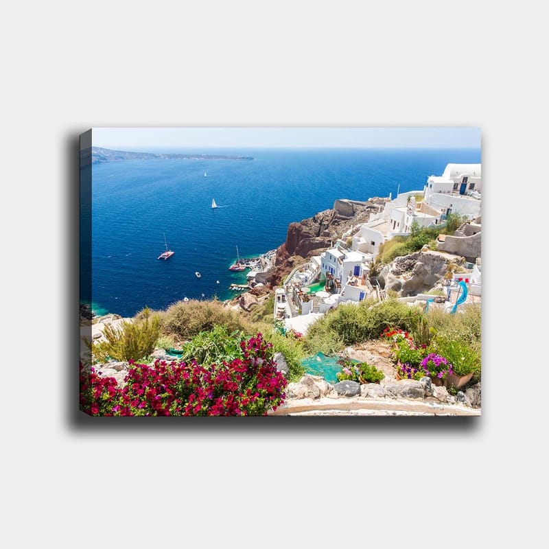 Lerretsbilde 70x100 cm - Vakker utsikt over Santorini med hvite hus og blomster som pryder klippene ved havet, Blå / Hvit / Grønn