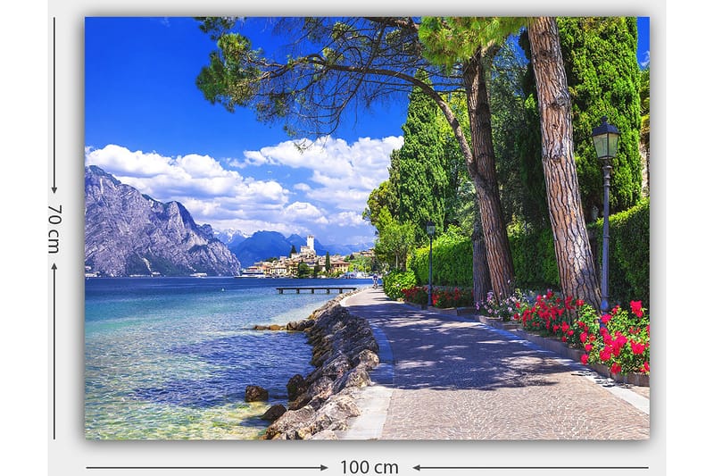Lerretsbilde 70x100 cm - Vakker promenade med trær og blomster ved en innsjø, omgitt av fjell og en pittoresk by i bakgrunnen - Blå / Grønn / Rød - Innredning - Bilder & kunst - Lerretsbilder
