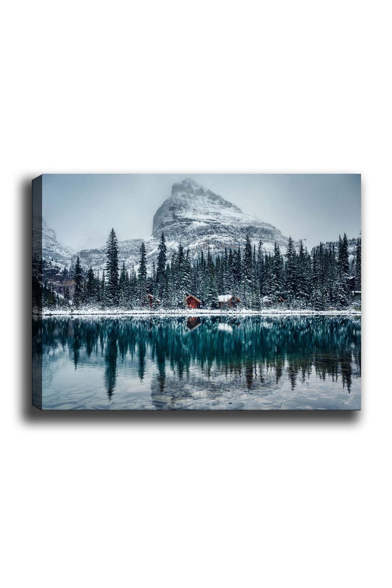 Lerretsbilde 70x100 cm - Vinterlandskap med snødekte fjell og en speilblank innsjø omgitt av grantrær og røde hytter, Mørk grønn / Blå / Hvit