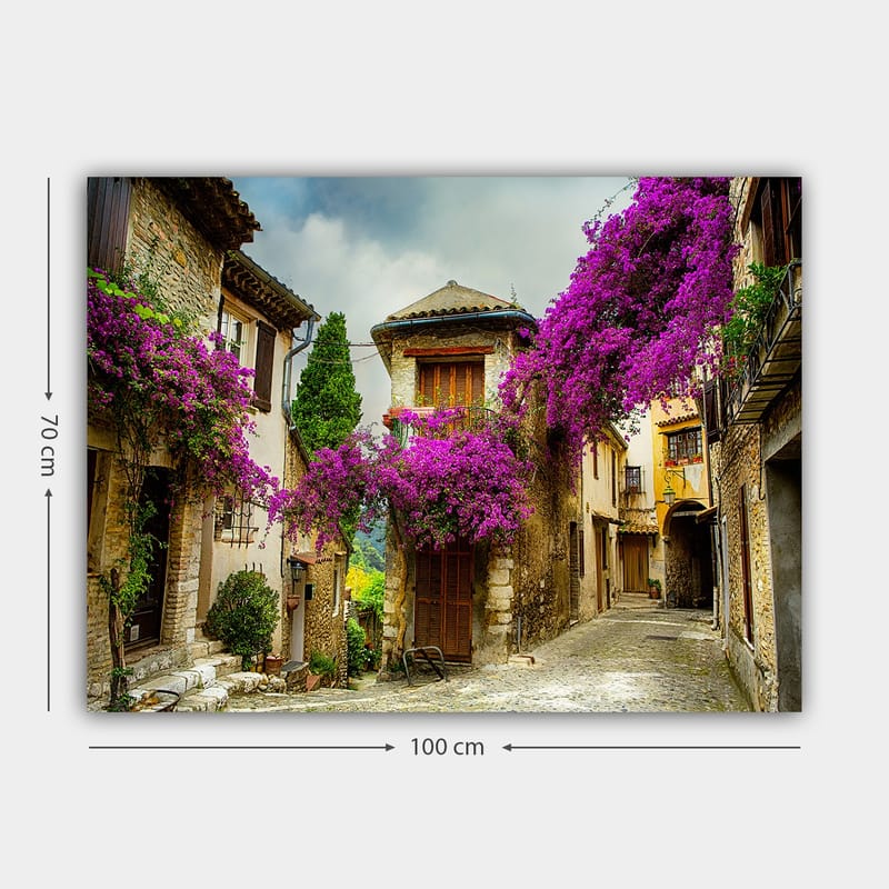 Lerretsbilde 70x100 cm - Pittoresk smug omgitt av fargerike blomster i sjarmerende landsbymiljø - Lilla / Grønn / Beige - Innredning - Bilder & kunst - Lerretsbilder