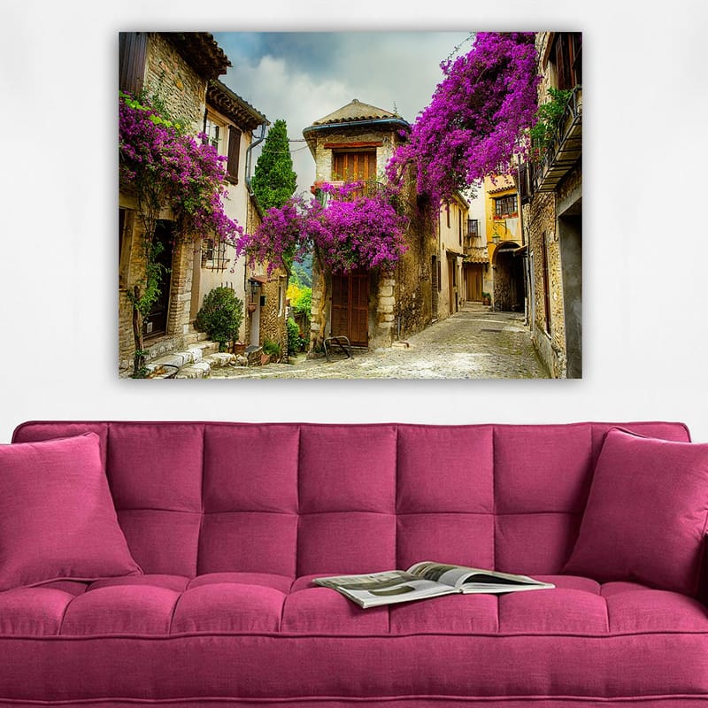 Lerretsbilde 70x100 cm - Pittoresk smug omgitt av fargerike blomster i sjarmerende landsbymiljø - Lilla / Grønn / Beige - Innredning - Bilder & kunst - Lerretsbilder