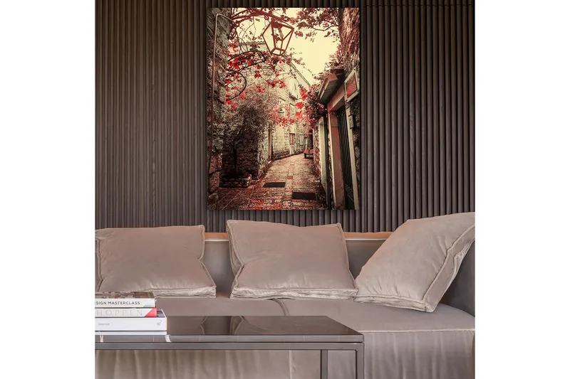 Lerretsbilde 70x100 cm - Pittoresk smug omkranset av gamle bygninger og blomster i røde fargetoner, Rød / Beige