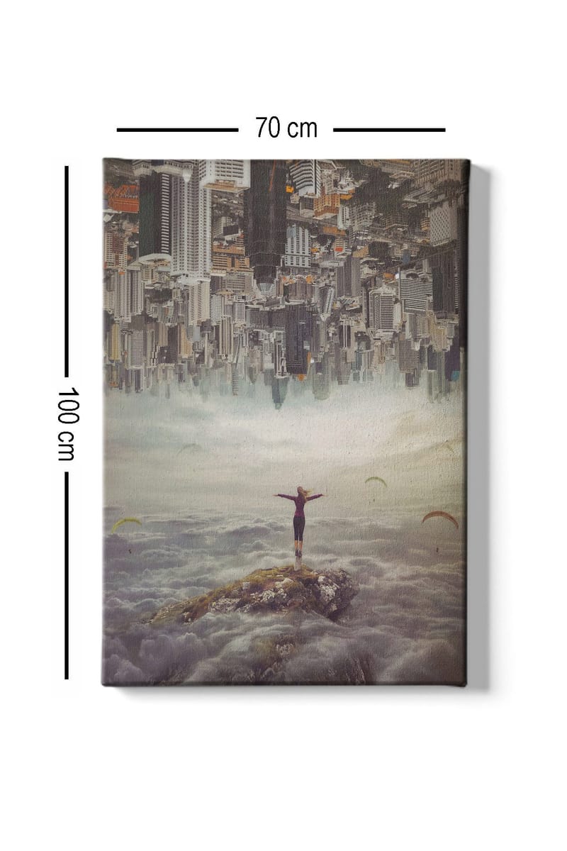 Lerretsbilde 70x100 cm - Person som står med utstrakte armer på en klippe over skyene, med en by i bakgrunnen som er opp ned - Grå / Beige / Mørk blå - Innredning - Bilder & kunst - Lerretsbilder