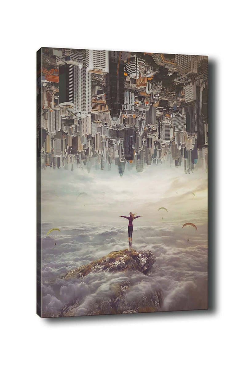 Lerretsbilde 70x100 cm - Person som står med utstrakte armer på en klippe over skyene, med en by i bakgrunnen som er opp ned, Grå / Beige / Mørk blå