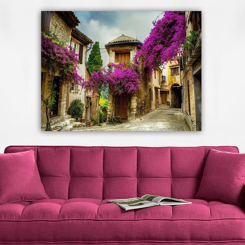 Lerretsbilde 70x100 cm - Pittoresk smug omgitt av fargerike blomster i sjarmerende landsbymiljø - Lilla / Grønn / Beige - Innredning - Bilder & kunst - Lerretsbilder