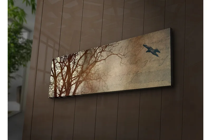 Lerretsbilde med LED-belysning 30x90 cm - Silhuett av et tre med en fugl i flukt mot en mykt tonet bakgrunn, Mørk brun / Beige / Svart