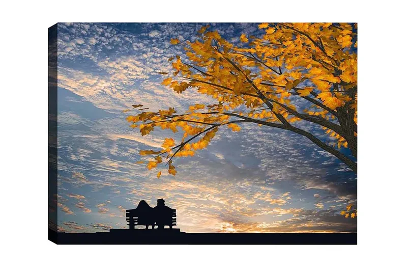 Lerretsbilde - Silhuett av et par som sitter på en benk under et tre med gyldne høstblader, Gull / Blå / Svart